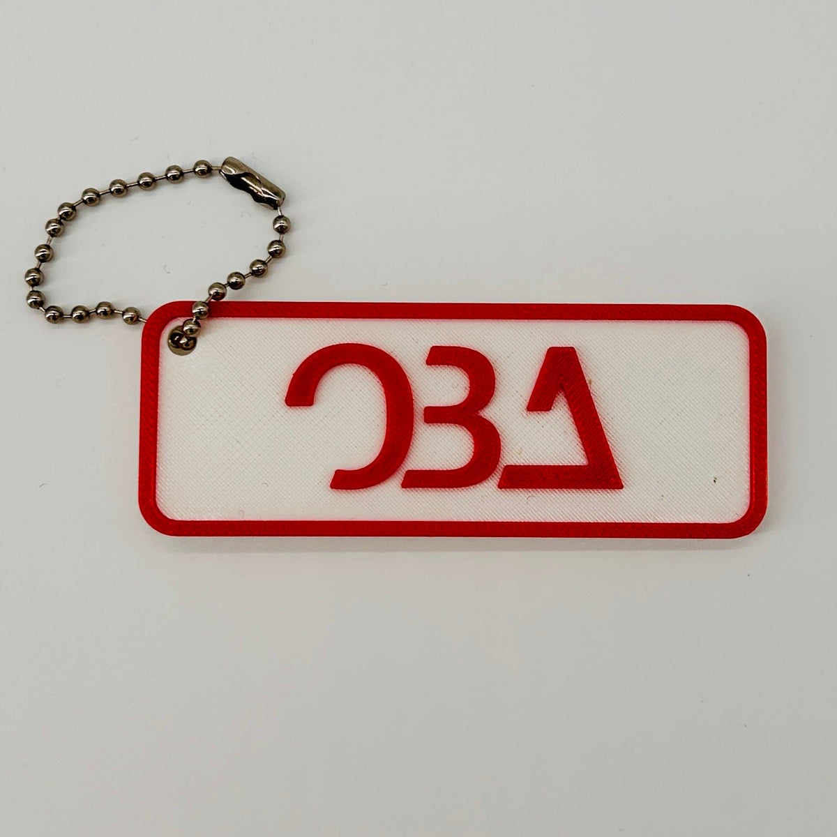 A rectangular white keychain with a red border and red OBA logo), attached to a silver ball chain, on a plain white background.