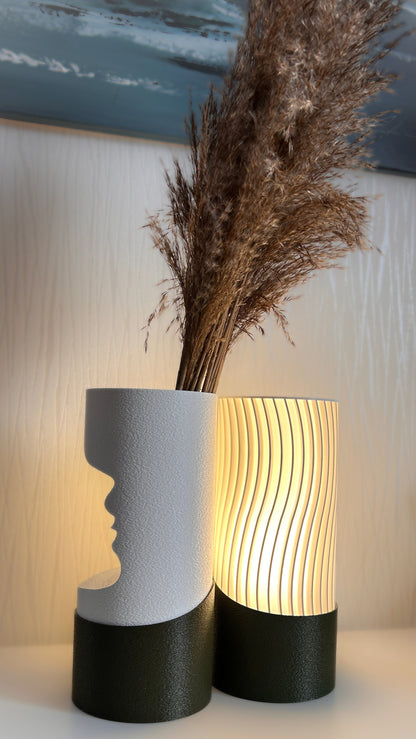 Two decorative vases with one featuring a face silhouette and the other with wavy design, on a light background.