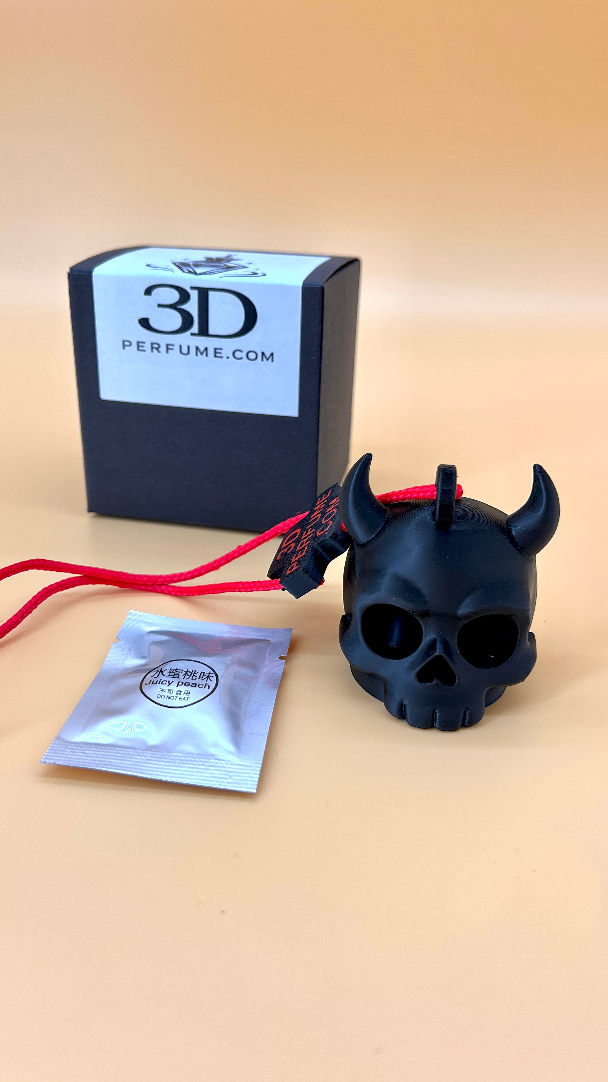 Black skull-shaped perfume bottle with red accents next to a 3D Perfume box and sachet on a beige background