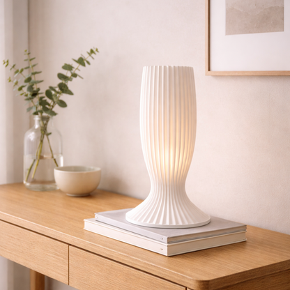 White textured table lamp on a wooden surface with a vase and plant in the background